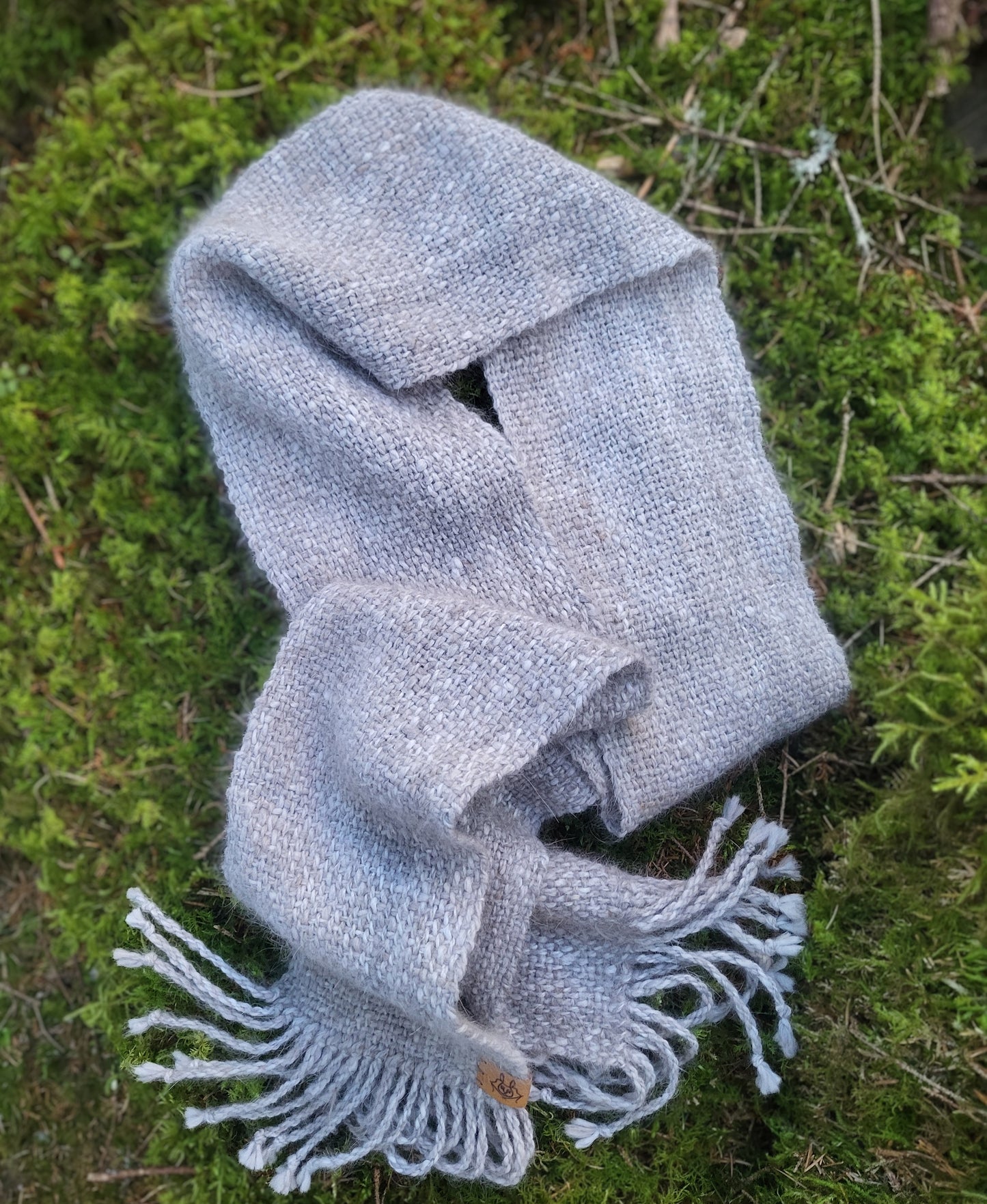 Håndvevd smalt angoraskjerf drapert på mosebunn i skogen