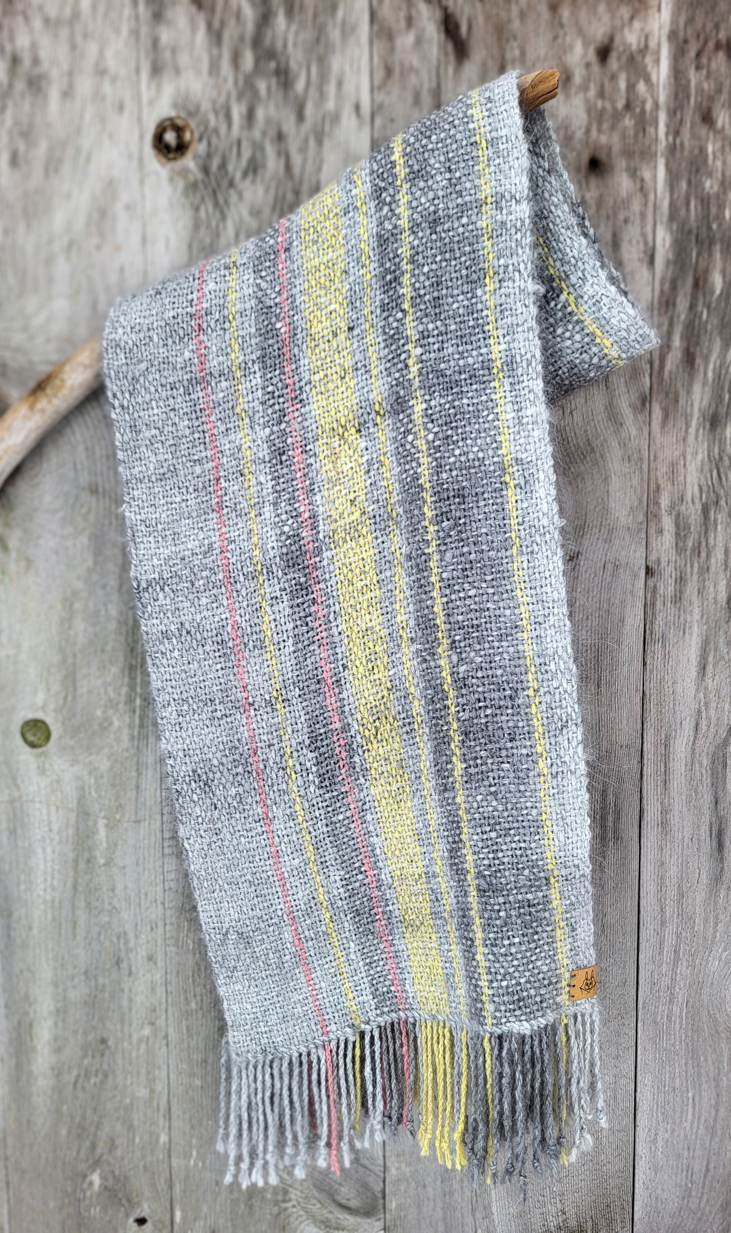 Håndvevd angoraskjerf i gråtoner med plantefarget striper drapert over trepinne med rustikk gammel dør som bakgrunn