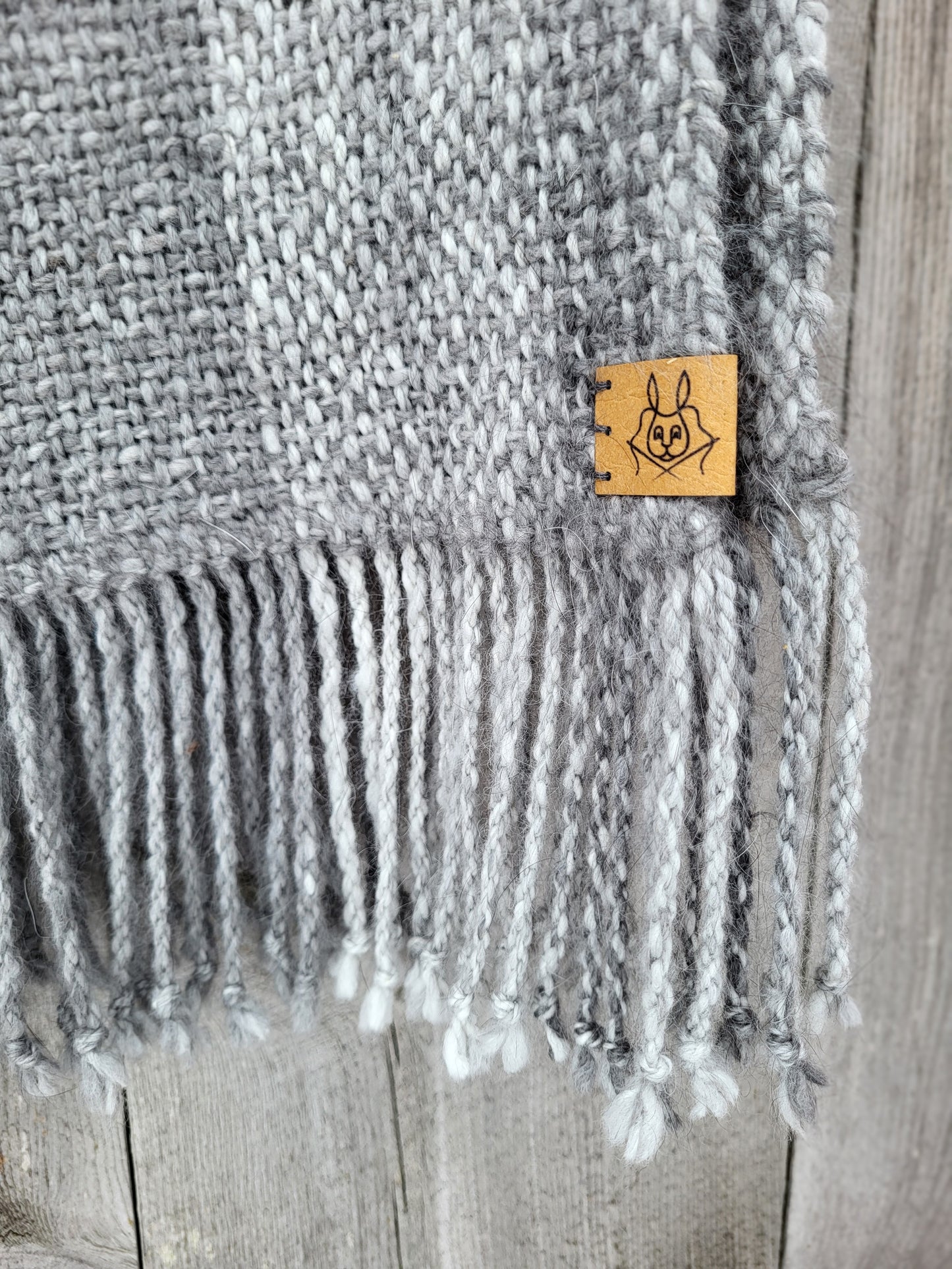 Nærbilde av logolapp Rytne Angora, med frynser, håndvevd angoraskjerf vevd i håndspunnet angoragarn fra egne kaniner
